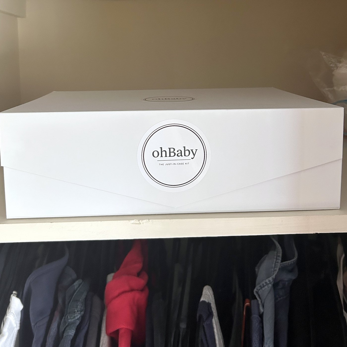 Oh Baby Kit box waiting on a closet shelf above a rail of hanging clothes.
