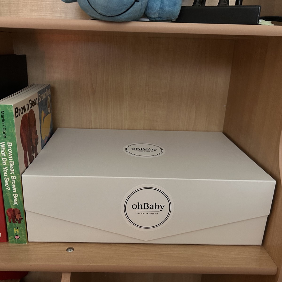 Oh Baby Kit box stored on a wooden shelf beside children's books.
